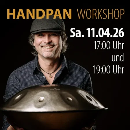 Sympathischer, lächelnder Mann mit Hemd und Schiebermütze hält eine Handpan in beiden Händen